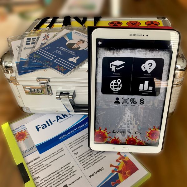 Umfangreiches Spielequipment für den Betriebsausflug: Einsatzbereites Tablet, gedruckte Fall-Akte, Agentenausweise für das Team und ein verschlossener Koffer für das Outdoor Escape Game Mission Antiserum.